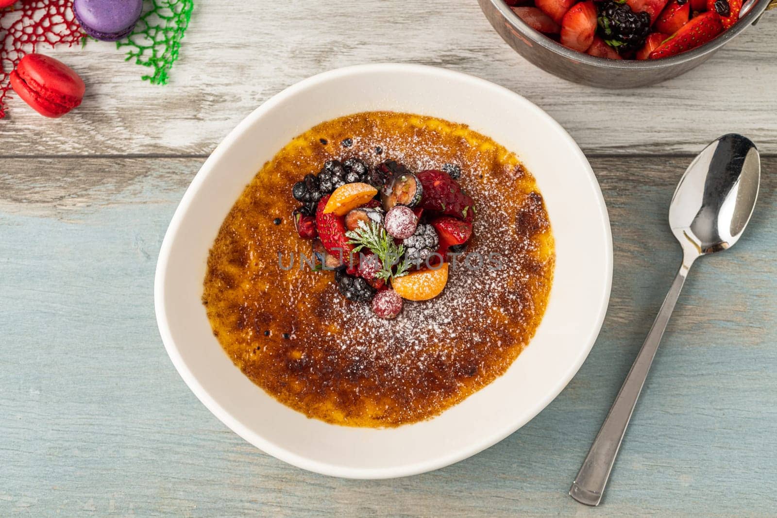 Creme brulee decorated with fruits and powdered sugar on a wooden table by Sonat