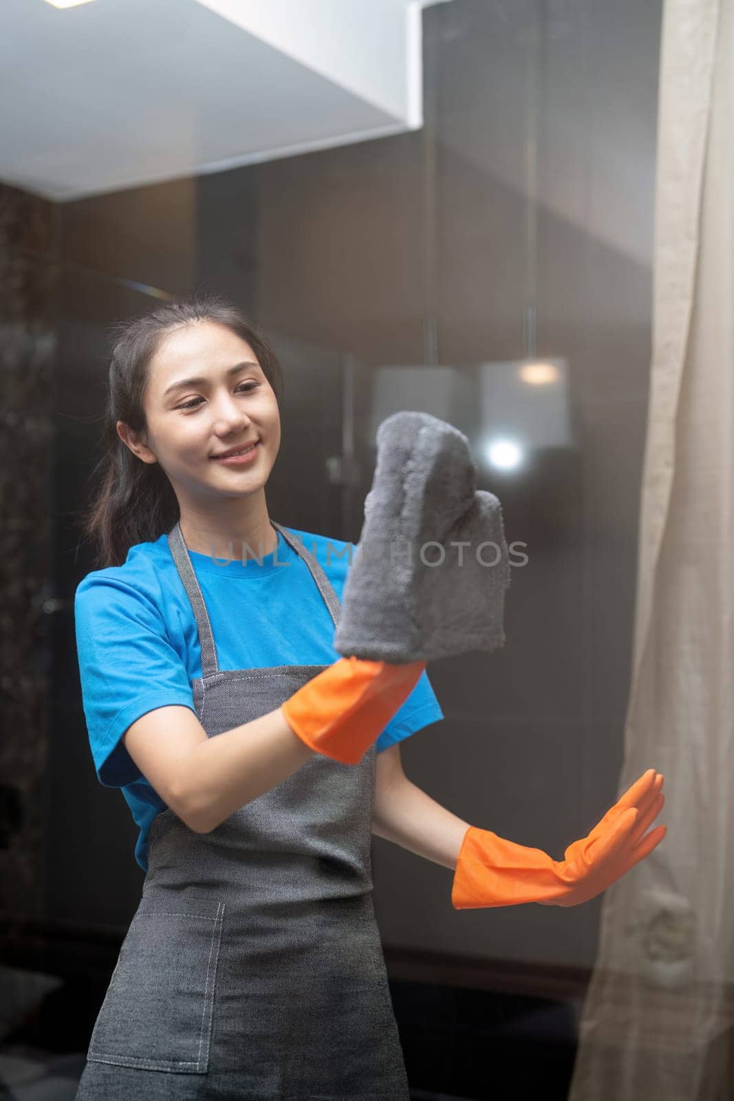 Asian woman cleaning the glass in the apartment. Cleaning staff maintain cleanliness in with towel and spray detergent by nateemee