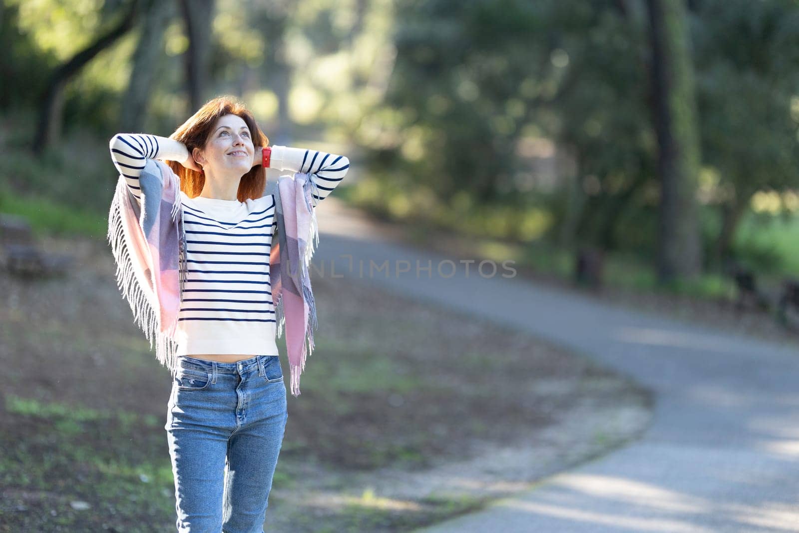 A woman wearing a striped shirt and jeans is walking down a path by Studia72