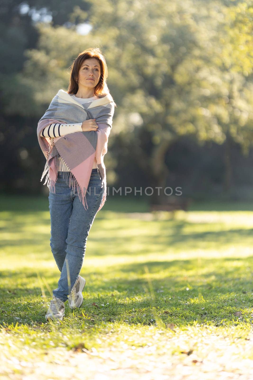 A woman wearing a multicolored scarf is walking in a park by Studia72