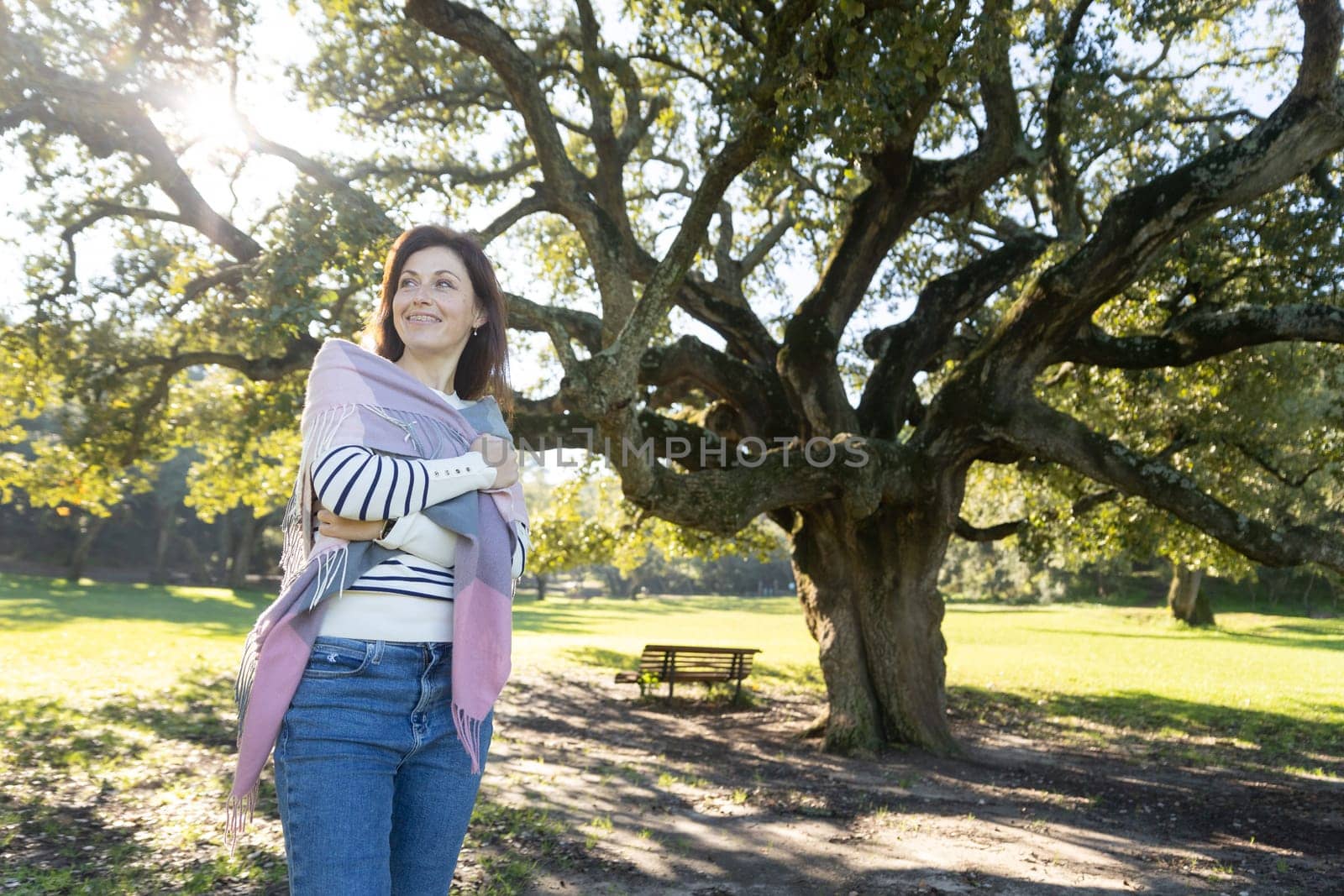 A woman is standing under a tree with a scarf wrapped around her shoulders by Studia72