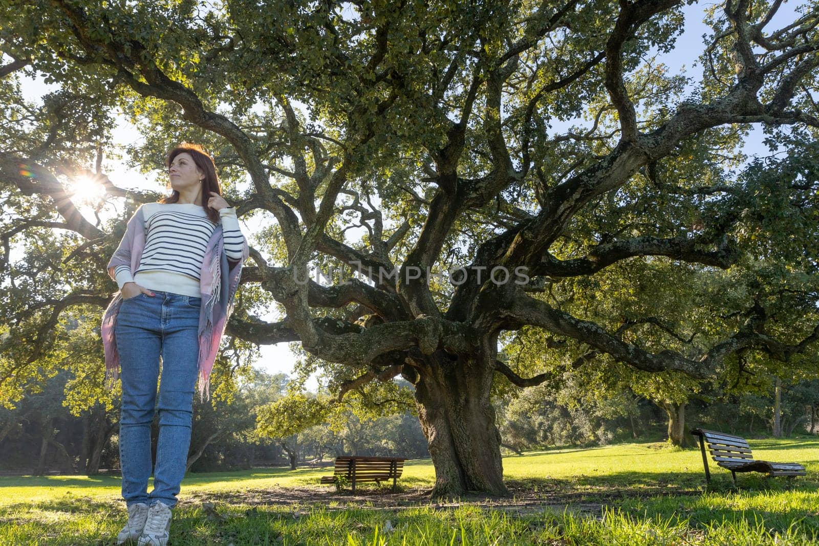 A woman stands in front of a large tree in a park by Studia72