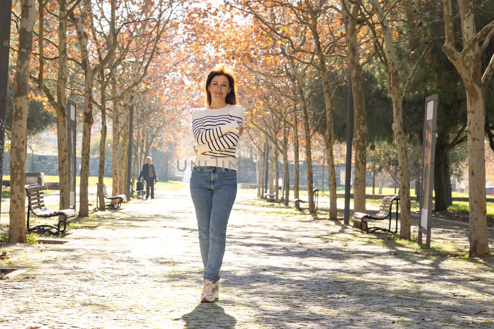 A woman is walking down a path in a park. She is wearing a white shirt and blue jeans