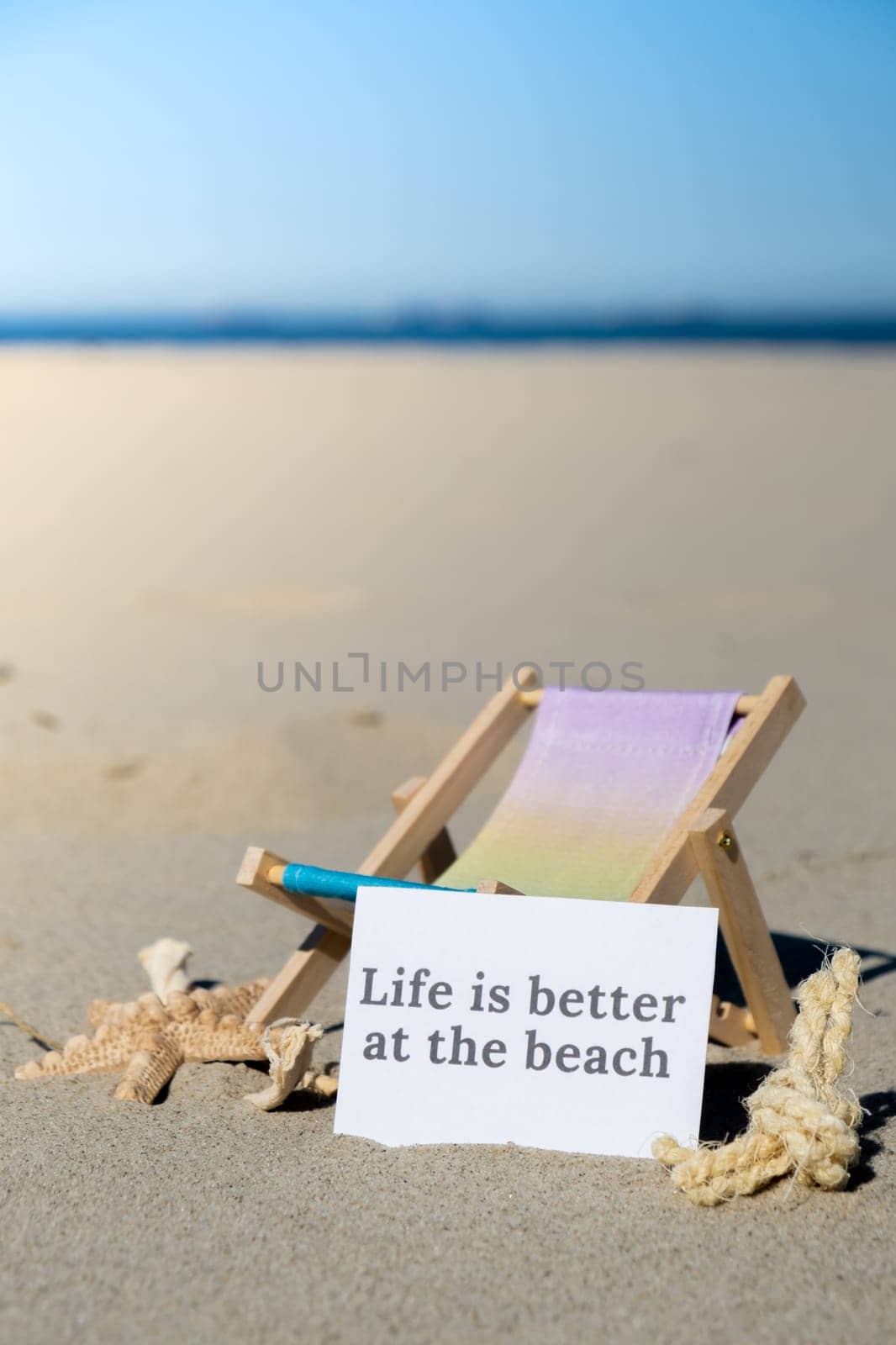 LIFE IS BETTER AT THE BEACH text on paper greeting card on background of beach chair lounge starfish summer vacation decor. Sandy beach sun. Holiday concept postcard. Travel Business concept