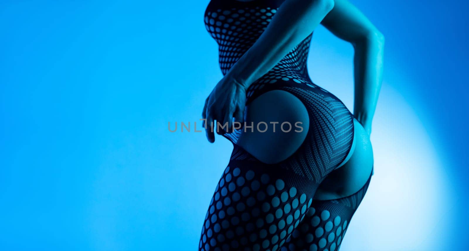 Sexy buttocks of a hot girl in close-up in erotic lingerie, mesh bodysuit with open crotch on a background copy paste in blue neon light