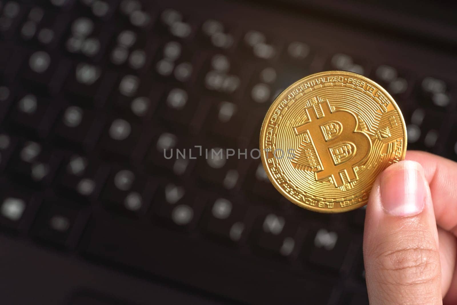 Woman hand holding golden coloured bitcoin coin over black laptop keyboard