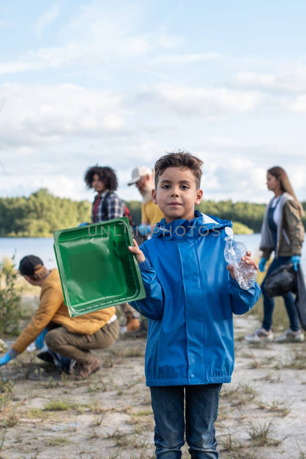 boy collects garbage plastic waste on the shore of a lake together with his volunteer friends by KaterinaDalemans