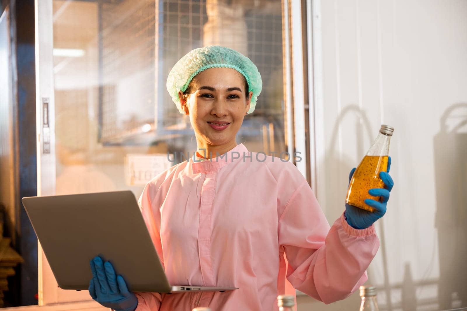 Female technician checks bottles on conveyor belt using laptop in beverage factory. Quality control manager ensures drink's perfection. Technology-driven liquid control is vital.