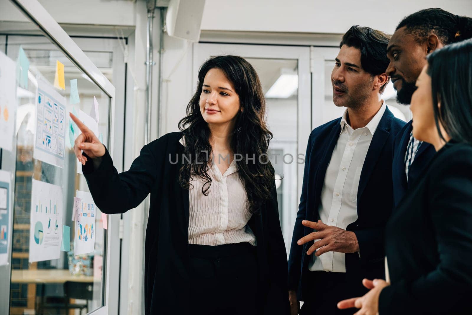 In a meeting setting, professionals creatively brainstorm and strategize on a transparent glass board. Teamwork, collaboration, and leadership are key to their success. by Sorapop