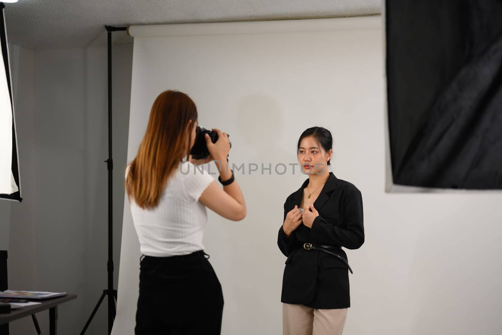 Fashion photographer taking picture of female model with digital camera in lighting studio by prathanchorruangsak