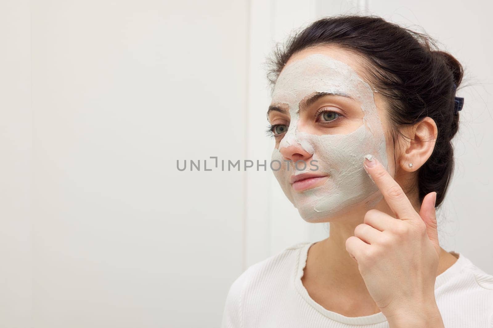 Caucasian woman looking in mirror and applying face mask by erstudio