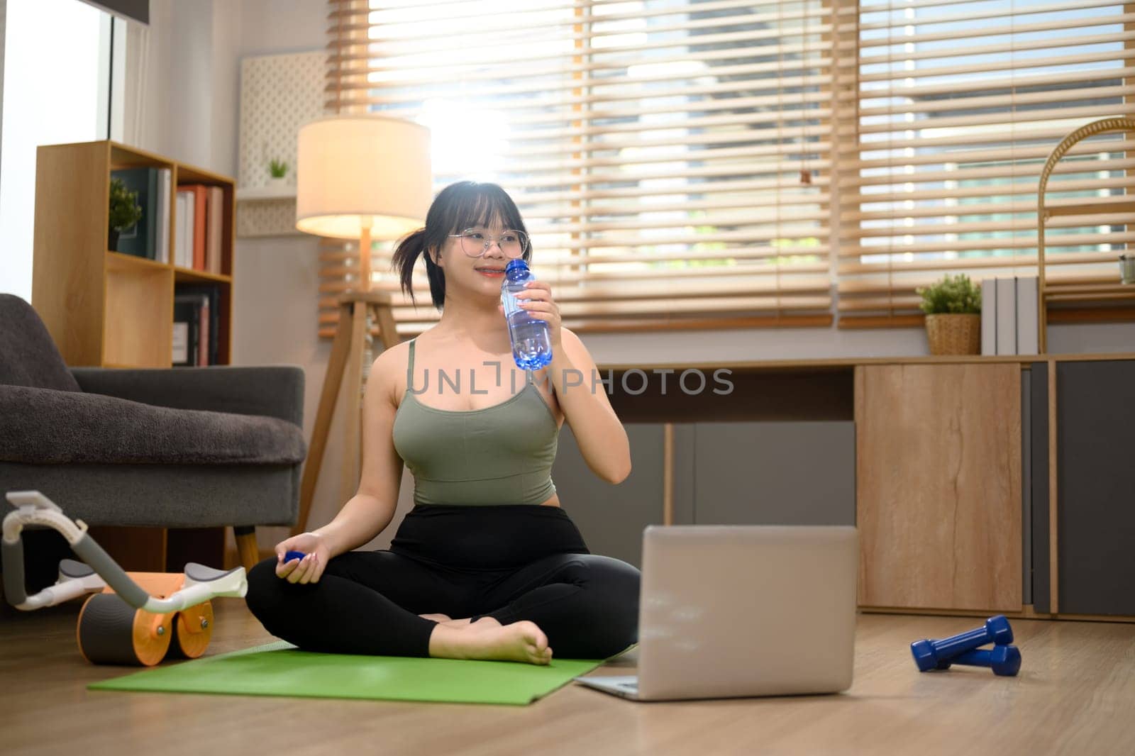 Happy young woman exercising at home and online fitness video tutorial on laptop by prathanchorruangsak