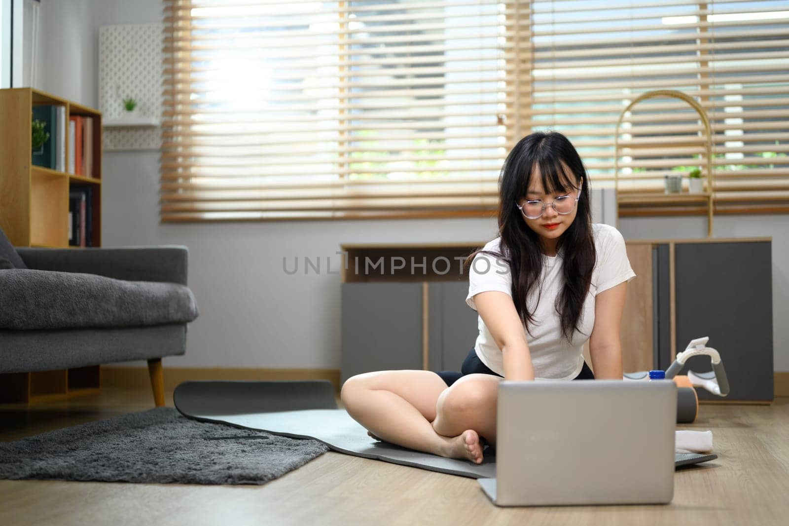 Happy young woman exercising at home and online fitness video tutorial on laptop.