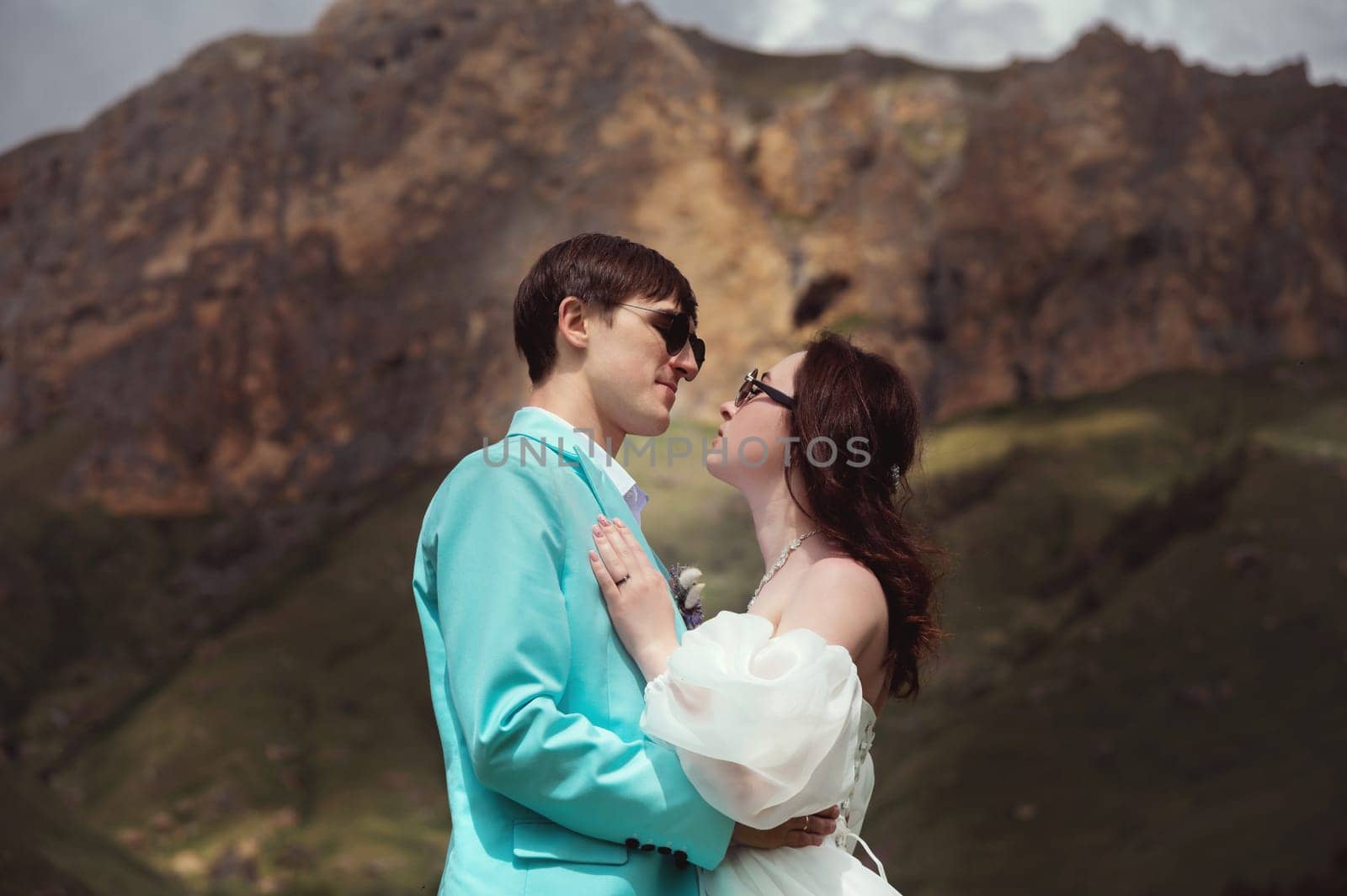 A young man and his wife stand in an embrace high in the mountains against the backdrop of epic rocks on a sunny day. Newlyweds wedding couple in the mountains by yanik88