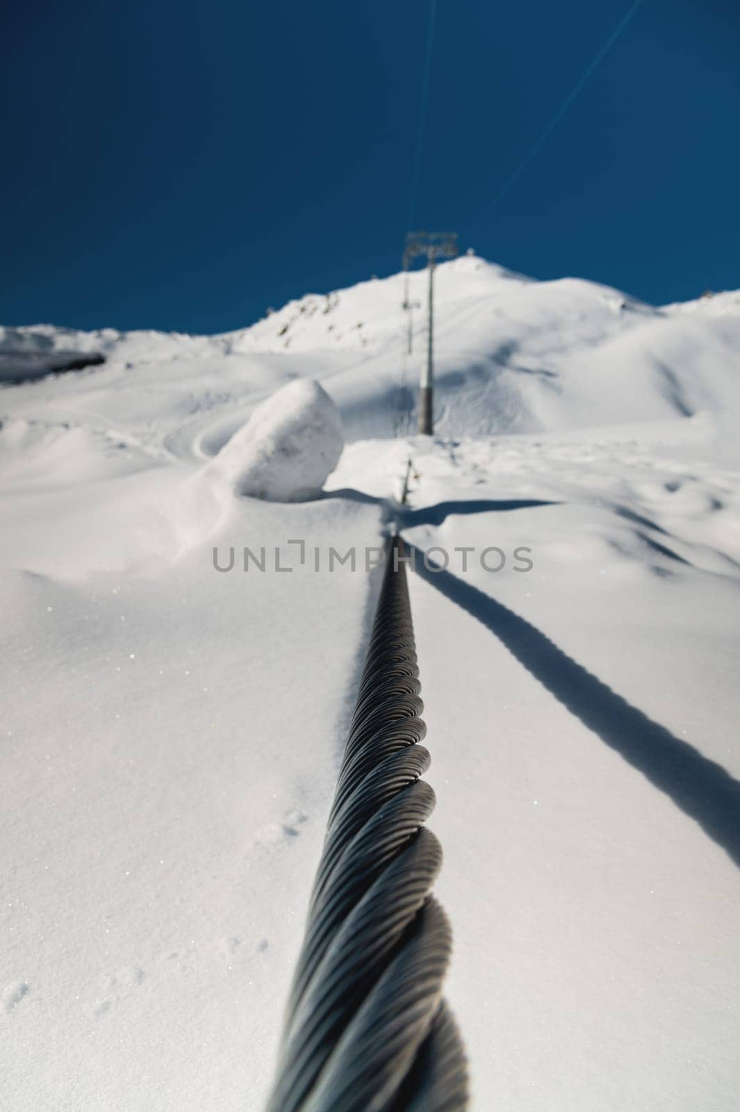 Steel cable of a cable car close-up. Rope texture. The path of the cable cabin against the backdrop of snow-capped mountains by yanik88