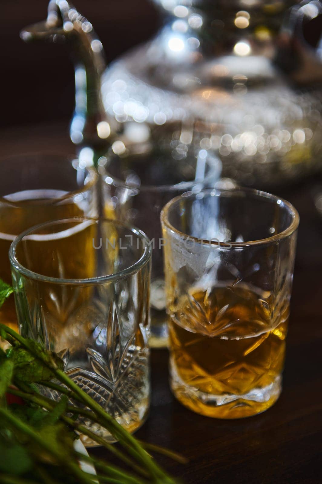 Close-up. Drinking glasses with traditional North African tea and silver teapot on blurred background. Moroccan mint tea with fresh menth