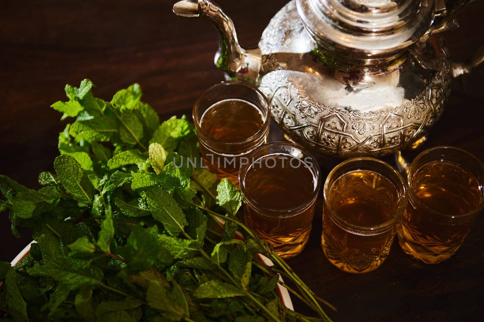 View from above Drinking glasses with fresh Moroccan tea with mint and silver traditional tea pot on wooden table. Enjoy a tea break in Moroccan traditions during Ftour Ftor at Ramadan or Aid Al Fitr