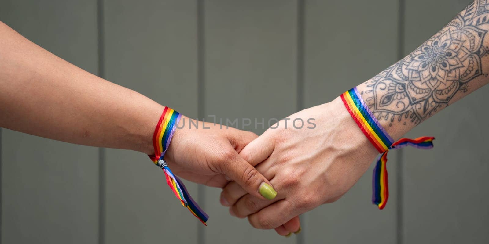 Hands of unrecognizable lesbian female couple with LGBT rainbow bracelet.