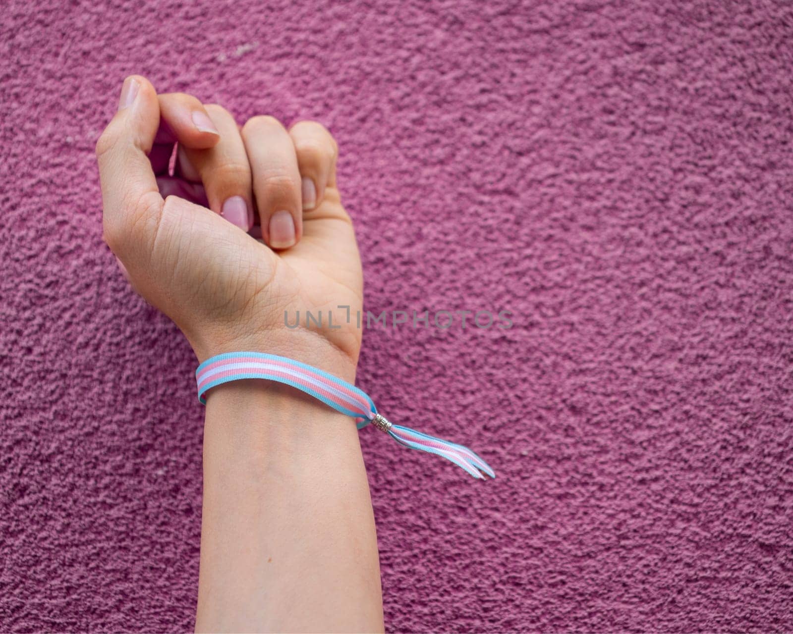 Close-up of closed fist with transgender bracelet over violet pink background. Copy space.