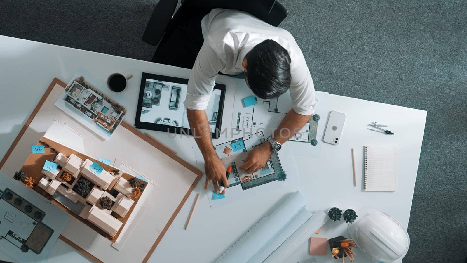 Top view of business man using tablet plan house design while sitting at meeting table with blueprint and equipment scatter around. Aerial view of civil engineer working at blueprint. Alimentation.