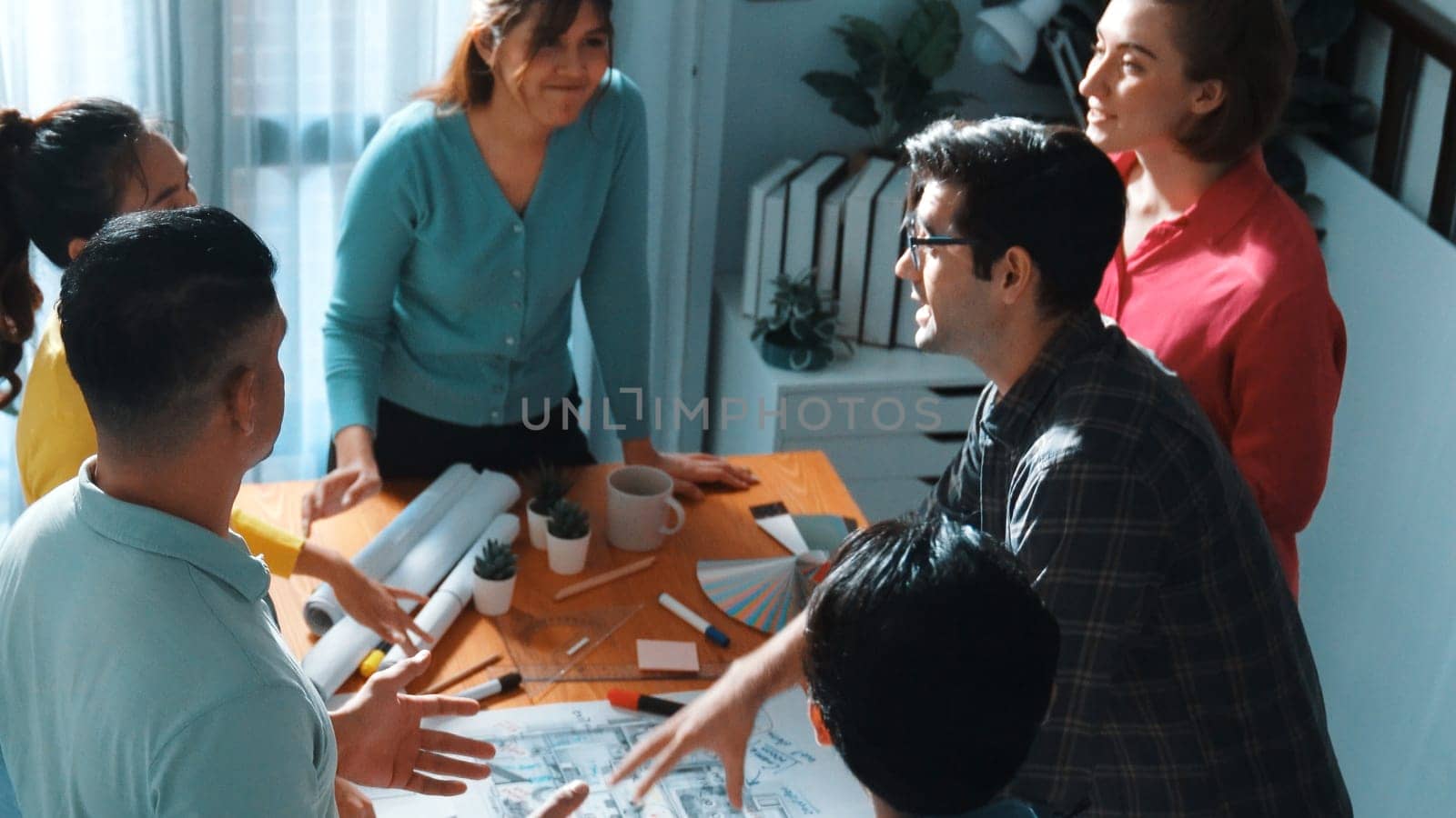 Top view of civil engineer team writing at blueprint at meeting table with color palettes. Group of smart diverse people planning and taking a note while manager looking at project plans. Symposium.