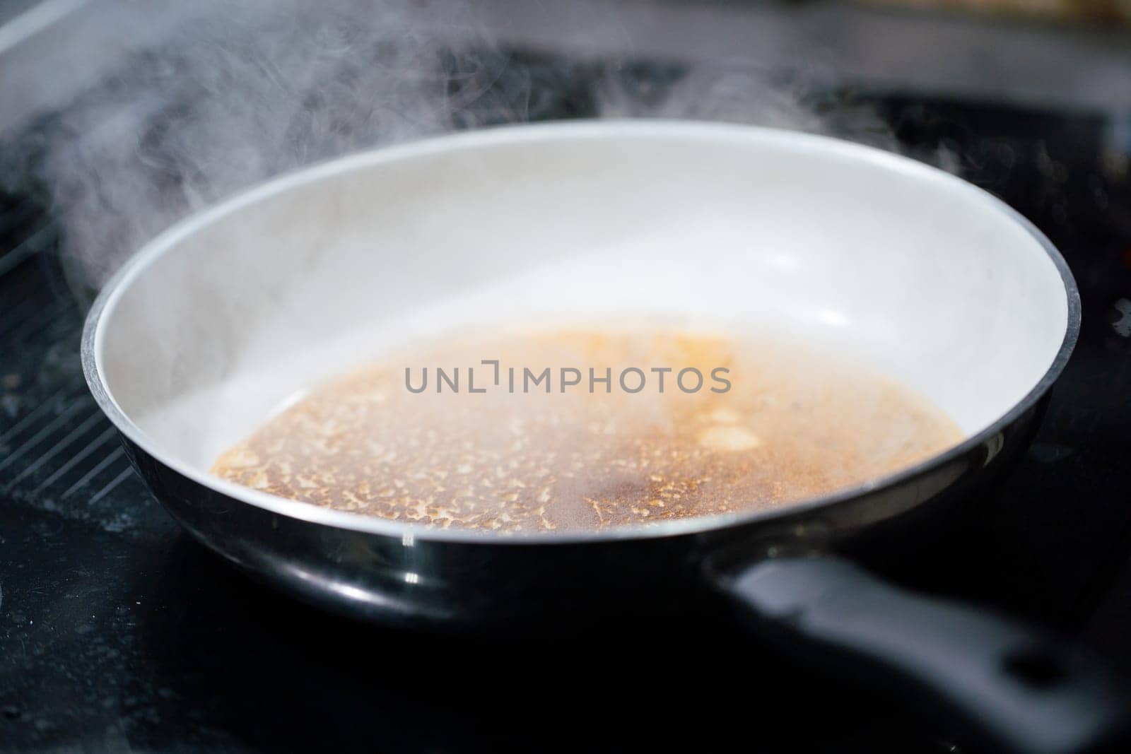 A large frying pan stands on the induction cooker and inside it is a pancake dough that is fried. The water evaporates from the pan.