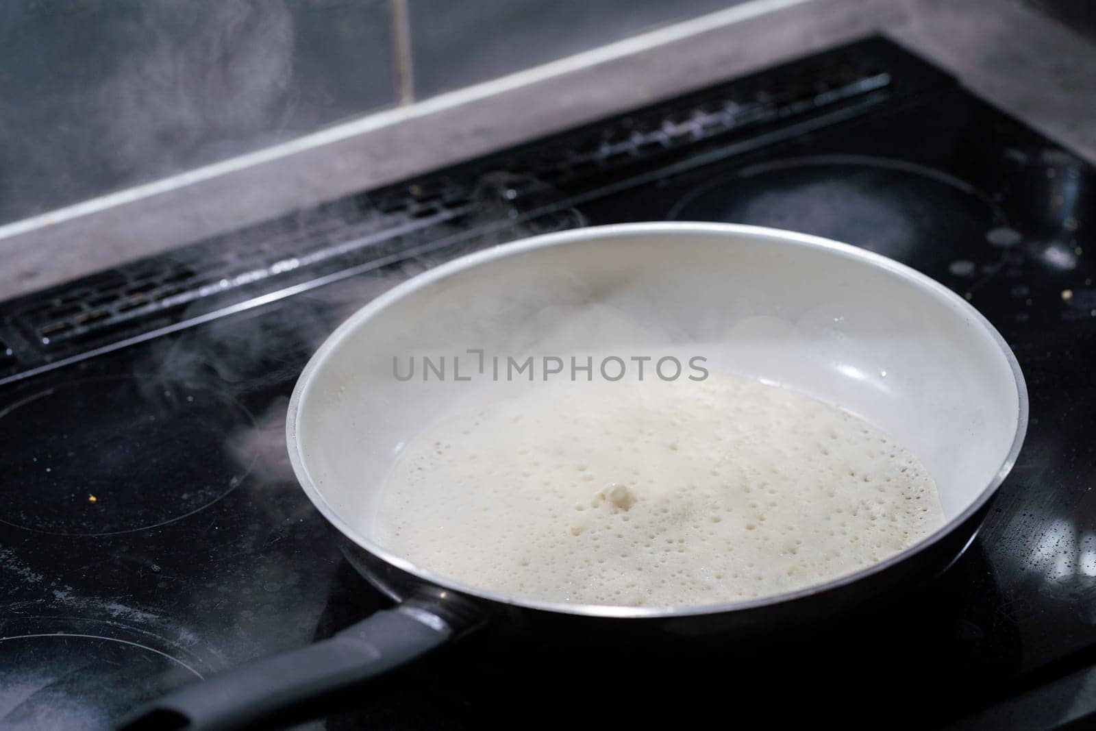 A large frying pan stands on the induction cooker and inside it is a pancake dough that is fried. The water evaporates from the pan.