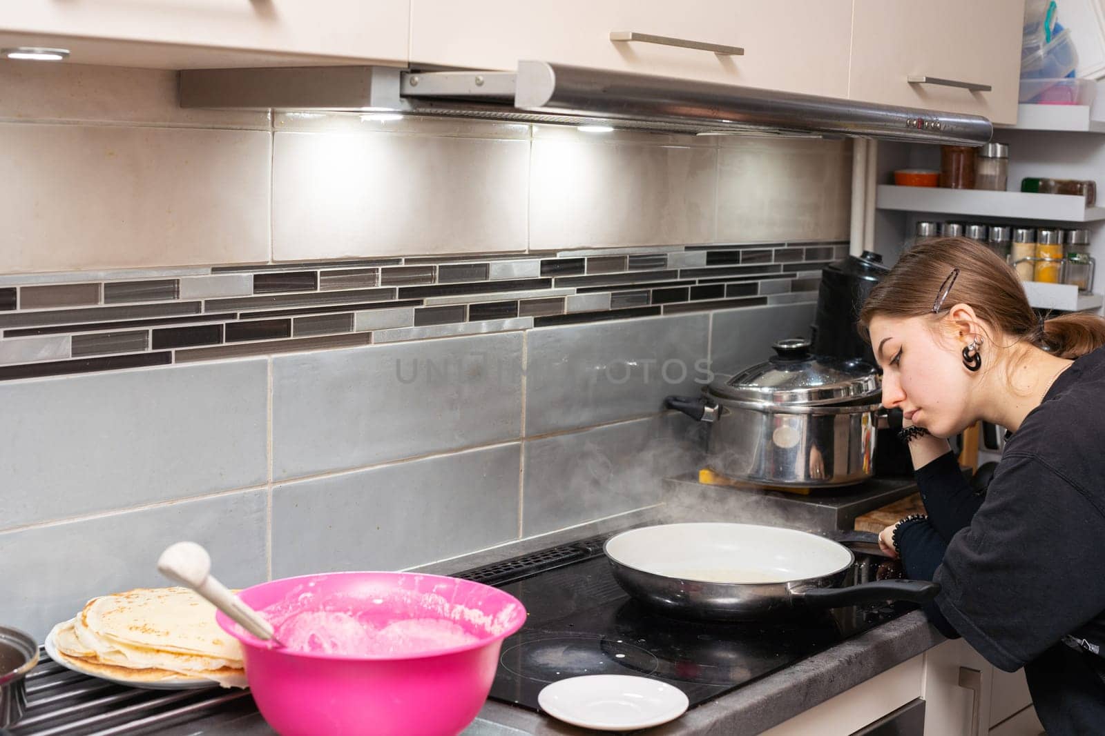 The teenager leaned her elbow on the kitchen counter and watched bored as the last piece was frying. Tasty homemade pancakes from a young woman's hand