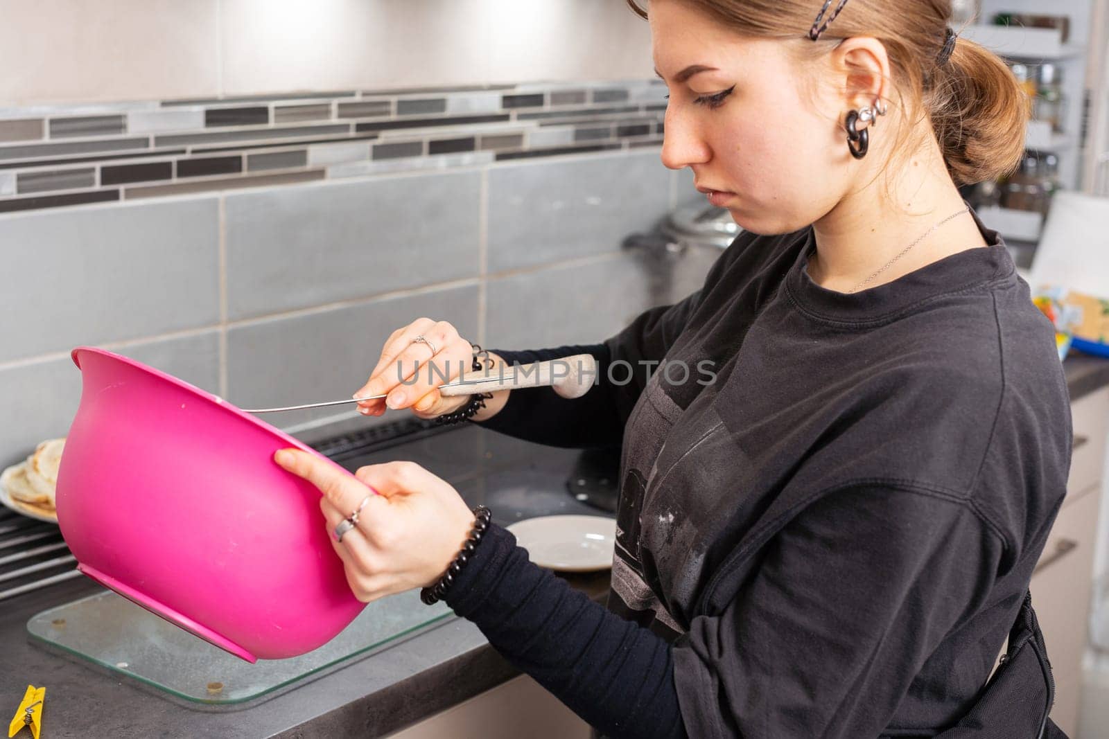 From a large pink bowl, the girl chooses the tip of the pancake dough. Tasty homemade pancakes from a young woman's hand.