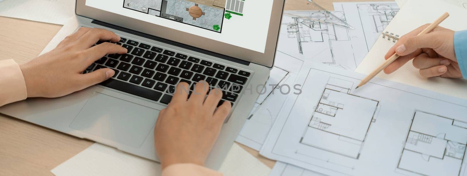 Eco house blueprint displayed on a laptop. Professional architect hand draws blueprint on meeting table with architectural document scatter around. Focus on hand. Closeup. Delineation.