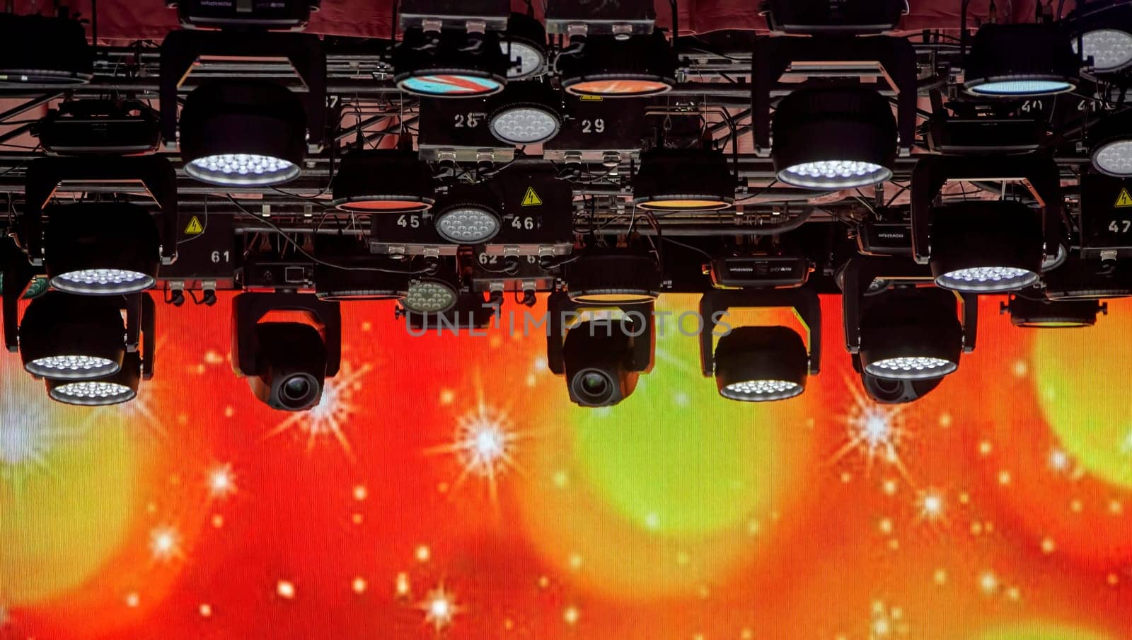 A lot of spotlights on the ceiling of the concert hall. Bright stage lights are on. The spotlights are arranged in a grid pattern. The stage is dark. The spotlights are creating a dramatic effect.