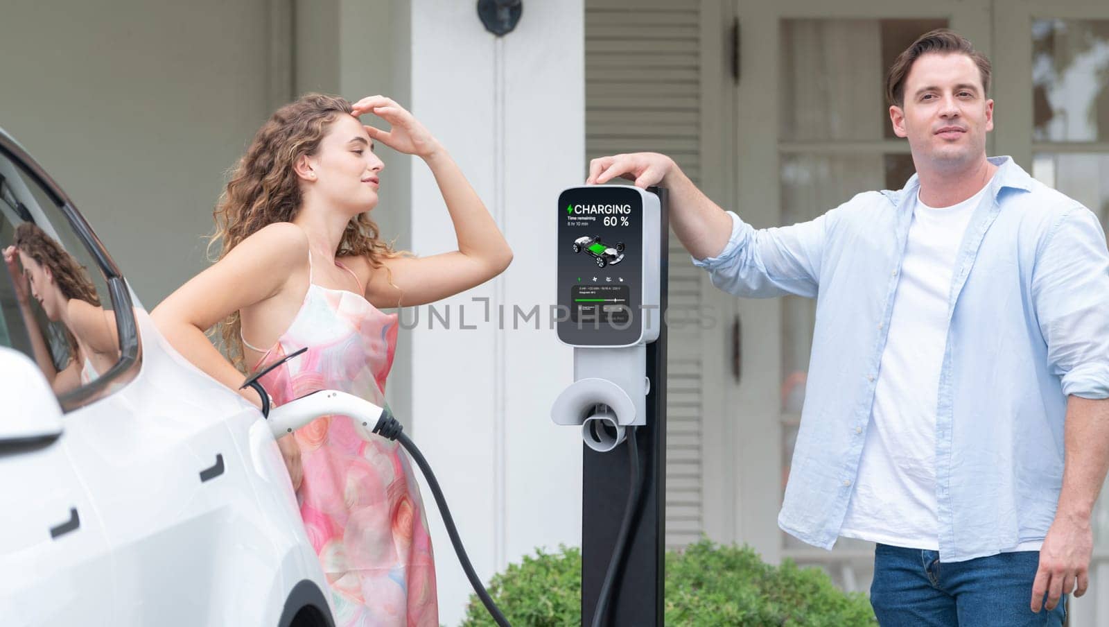 Happy and lovely couple with eco-friendly conscious recharging electric vehicle from EV home charging station. EV car technology utilized for residential home to future sustainability. Synchronos