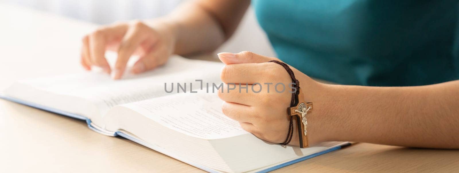 Cropped image of female reading a bible book while holding cross at wooden table with blurring background. Concept of hope, religion, faith, christianity and god blessing. Warm. Burgeoning.