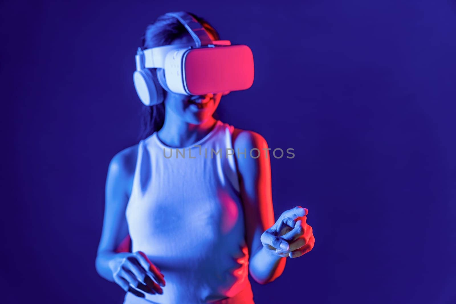 Smart female stand with surrounded by cyberpunk neon light wear VR headset connecting metaverse, futuristic cyberspace community technology. Woman using finger pointing virtual object. Hallucination.