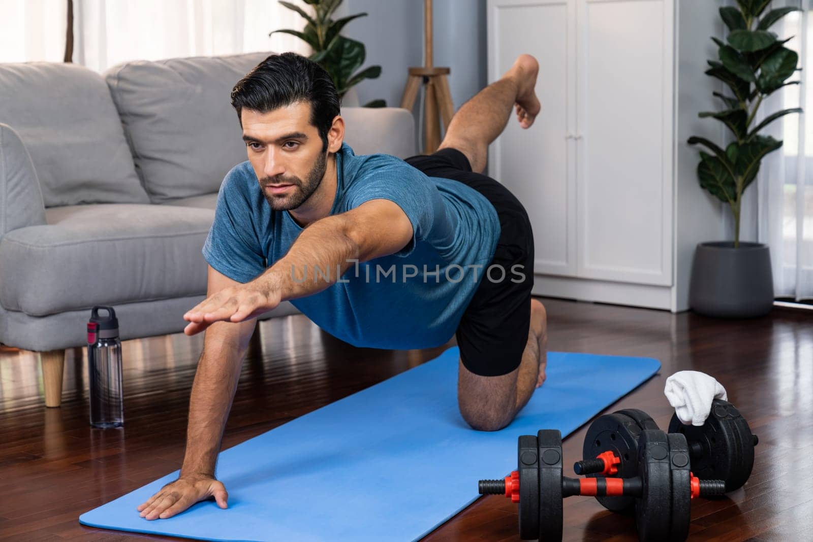 Flexible and dexterity man in sportswear doing yoga position in meditation posture on exercising mat at home. Healthy gaiety home yoga lifestyle with peaceful mind and serenity.