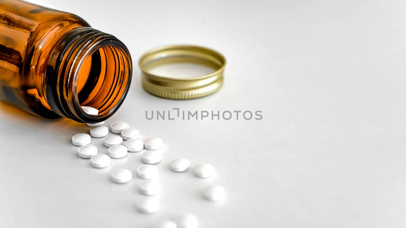 Scattered White Pills with Brown Glass Bottle on White Background, Copy Space, Close-Up, Healthcare Concept. by Laguna781