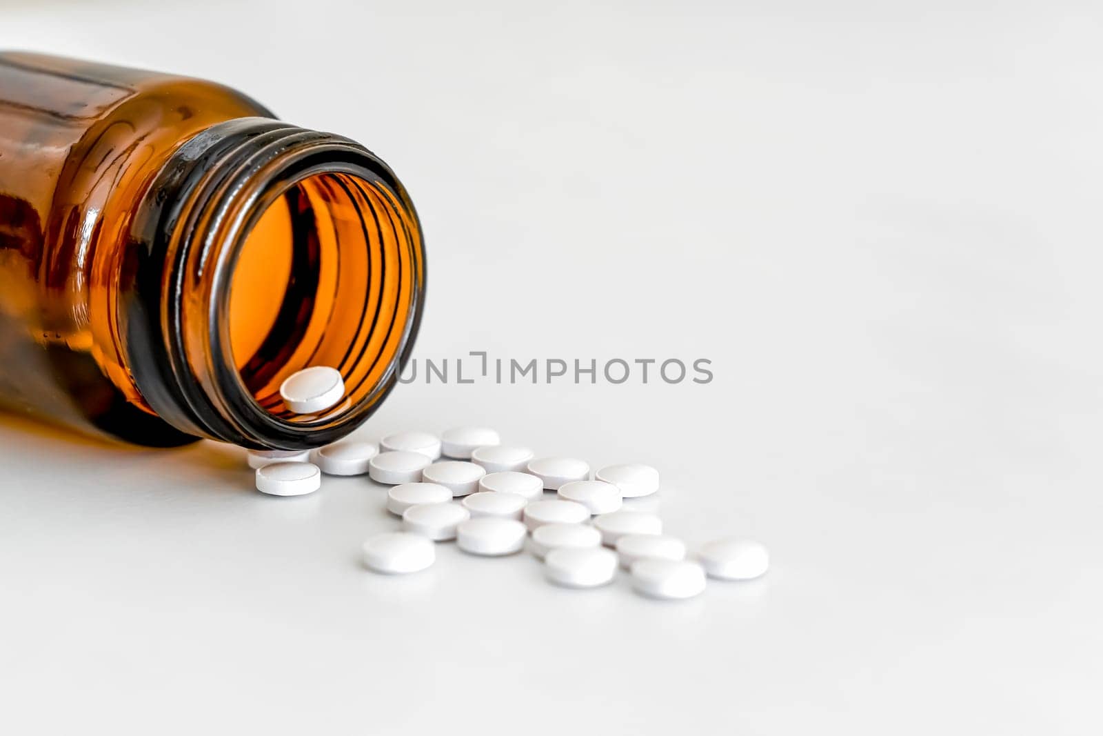 Scattered White Round vitamins and Brown Glass Bottle on White Background, Copy Space, Close-Up, Healthcare Concept.