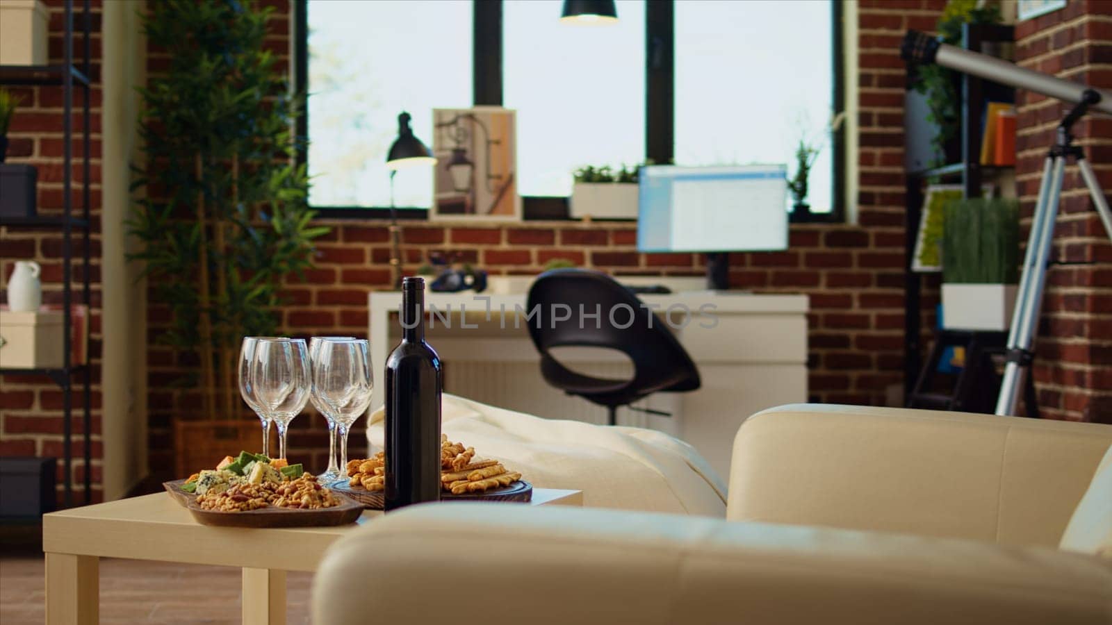 Panning shot of empty cozy apartment living room with appetizer platter and wine bottle on wooden table, awaiting guests to arrive. House interior with leather couch and TV running in background