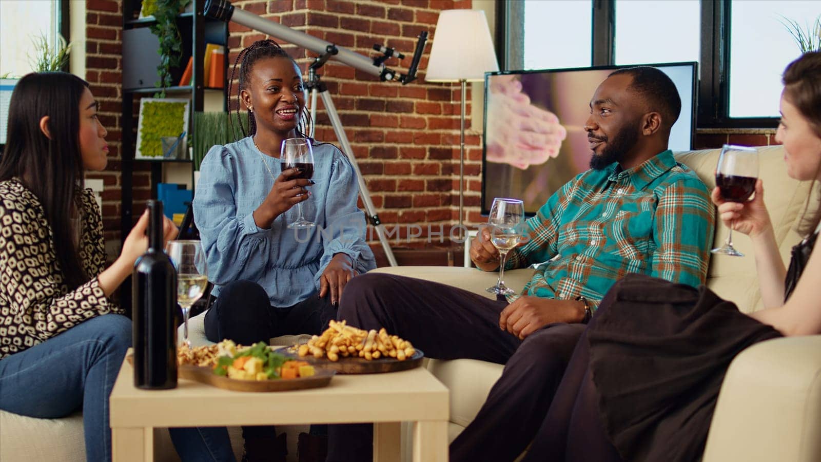 African american woman captivating friends at apartment party with compelling story. Guest making multiracial group of people laugh in stylish living room while drinking and eating