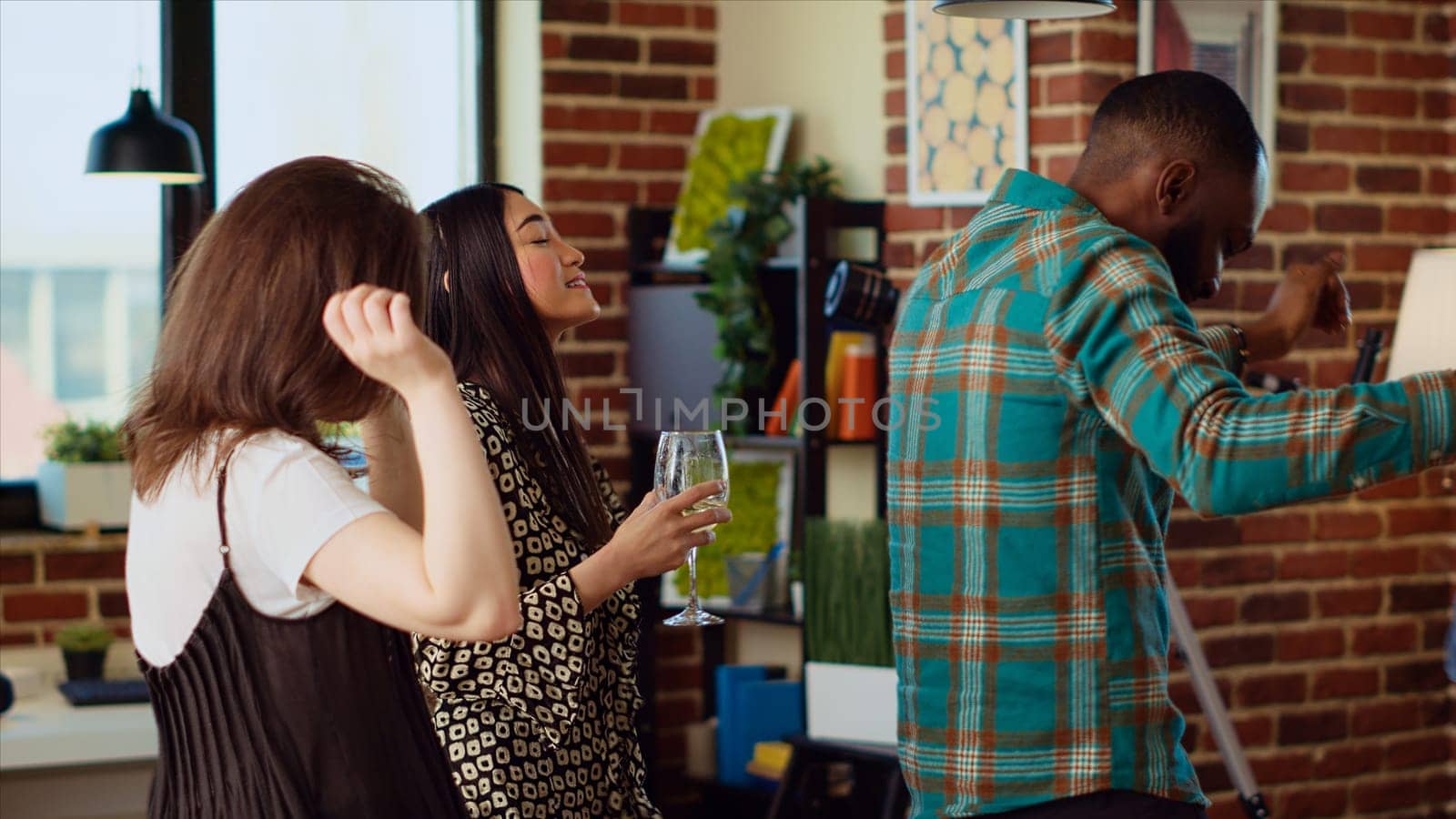 Happy friends dancing at house party while drinking wine and champagne, enjoying weekend. Inclusive group of people having fun indoors, doing dance moves to music in living room, close up