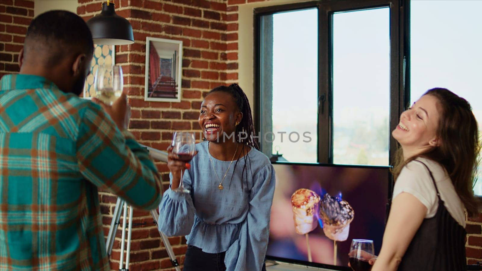 Young adults of various nationalities dancing at apartment party while drinking alcoholic beverages. Friends hanging around, having good time together while enjoying electronic songs in living room