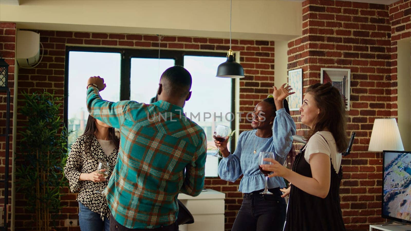 Multicultural mix of guests at apartment party sharing laughter and dance moves, creating vibrant atmosphere in living room. Happy friends dancing on electronic beats during weekend hangout