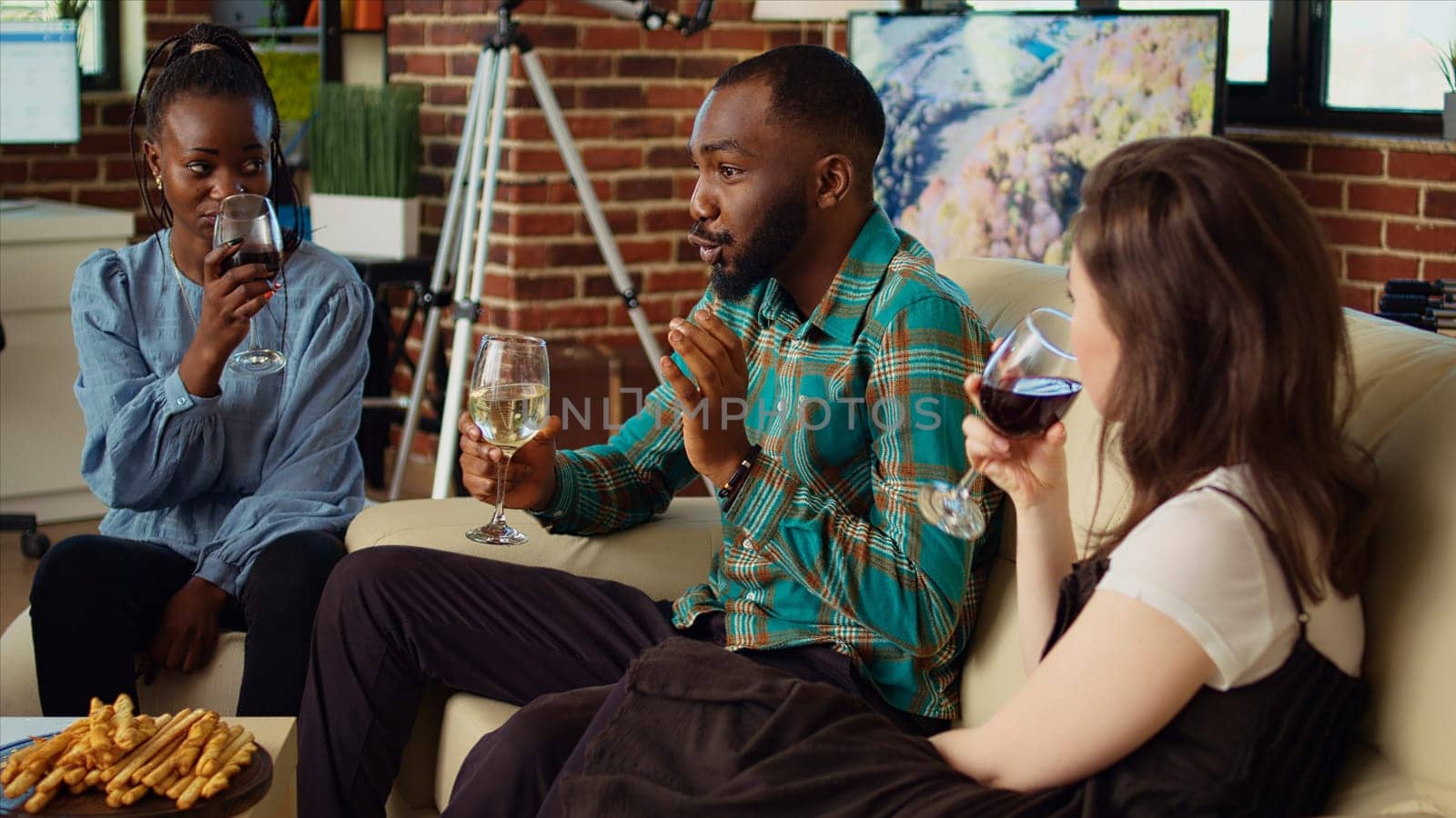 Diverse group friends celebrating african american man birthday, drinking alcohol and eating appetizers in apartment. Guests laughing and discussing at apartment gathering after gifting host presents