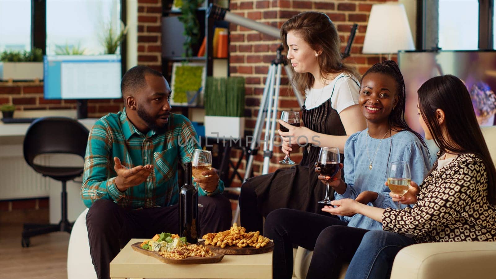 Diverse group friends celebrating asian woman birthday, drinking alcoholic beverages and eating gourmet cheese. Cheerful guests laughing in brick wall living room after gifting host presents