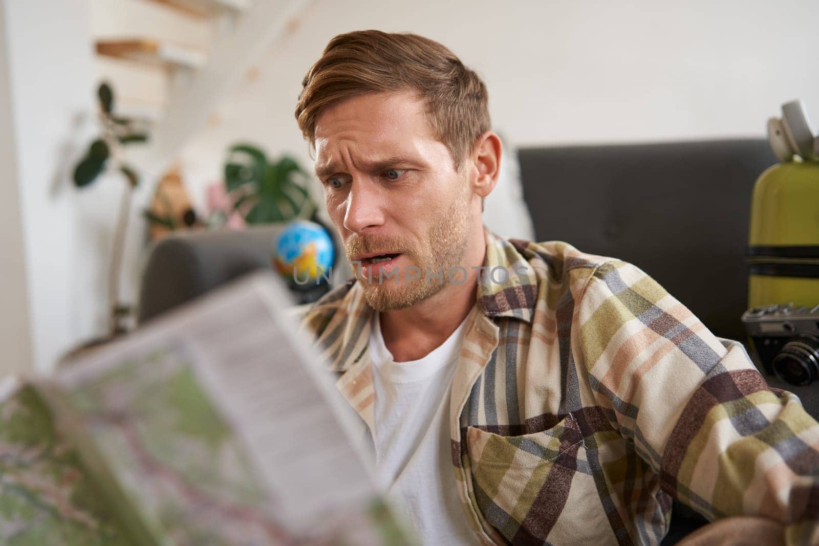 Portrait of confused guy looking at travel map, choosing route, going on holiday, plans to go on vacation. tourism concept