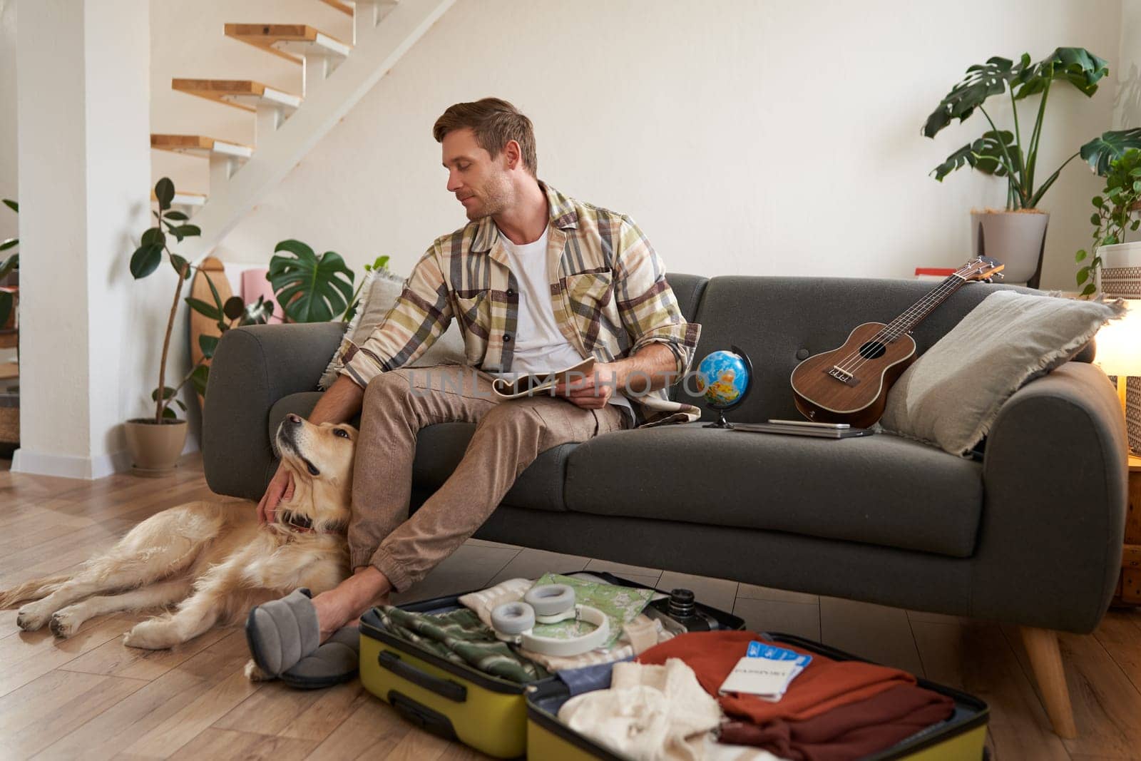 Portrait of young man packing for a trip, going on vacation, putting clothes inside suitcase, preparing for holiday.