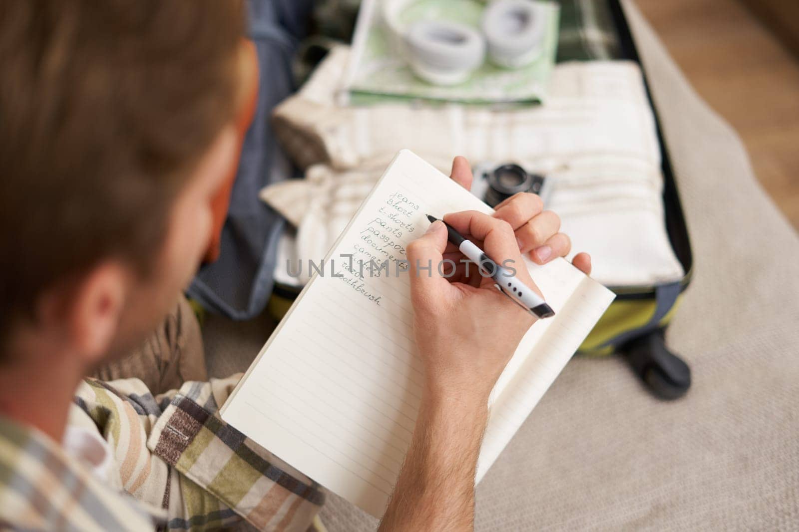 Close up portrait of man packing suitcase, making notes, check-list of items he wants to take on holiday, packing luggage by Benzoix
