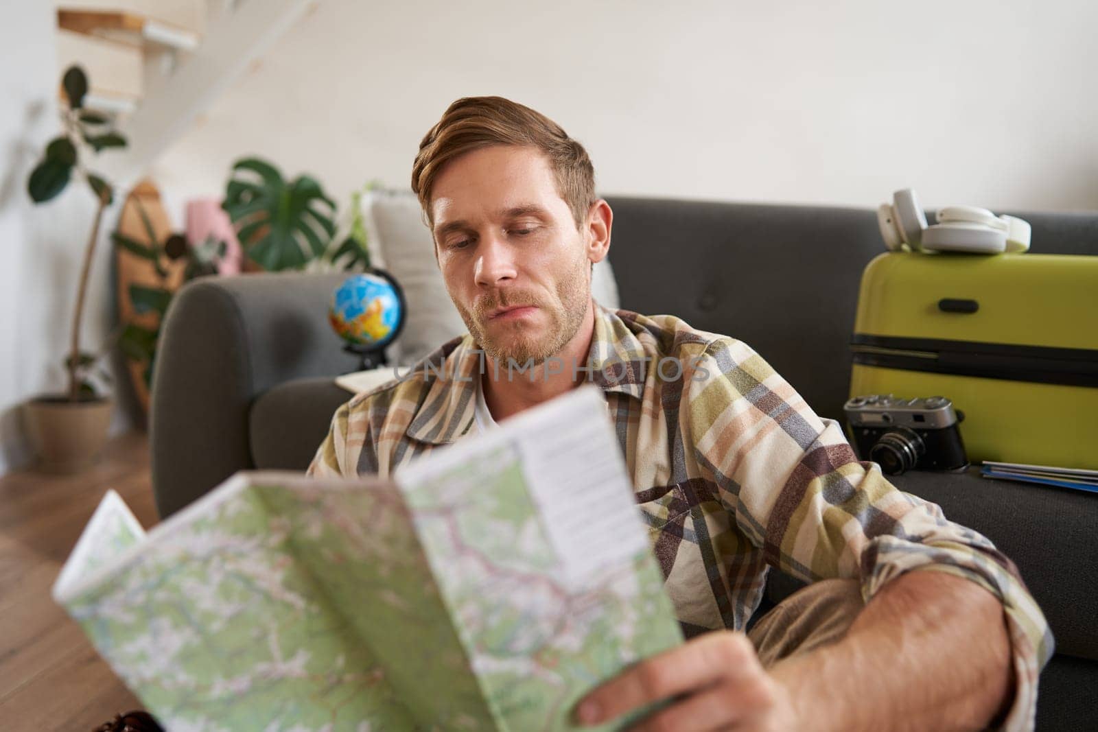 Portrait of handsome young man, traveller with suitcase, looking at paper map, choosing where to go on vacation, going on holiday, choosing route by Benzoix