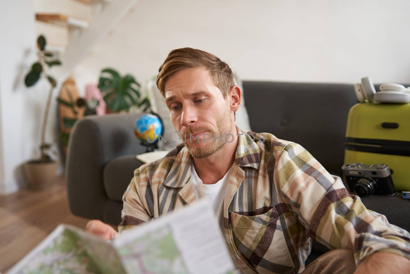 Portrait of man, traveller looks confused at map, studying the route to go on vacation or business trip. Tourism concept