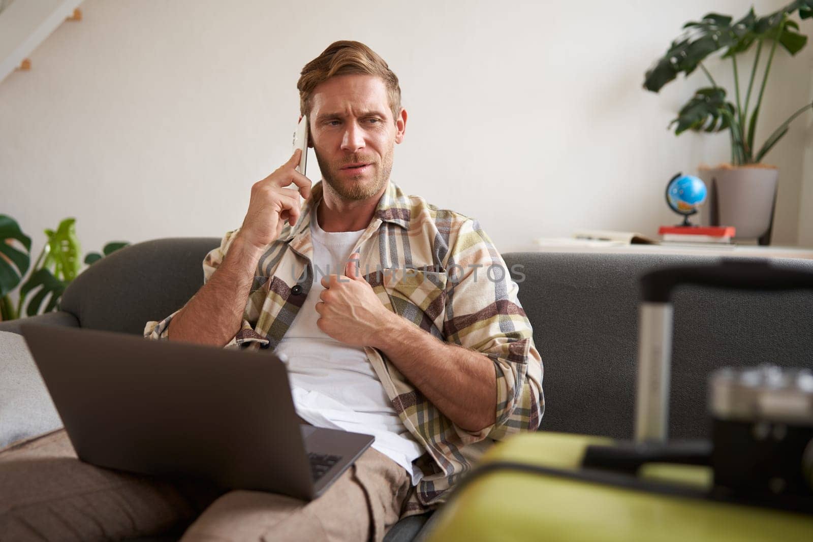 Portrait of man talking on mobile phone, tourist with laptop and suitcase answers telephone.